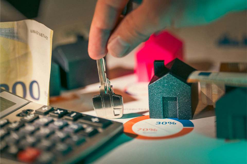 Hand holding keys with mini houses for property investment.