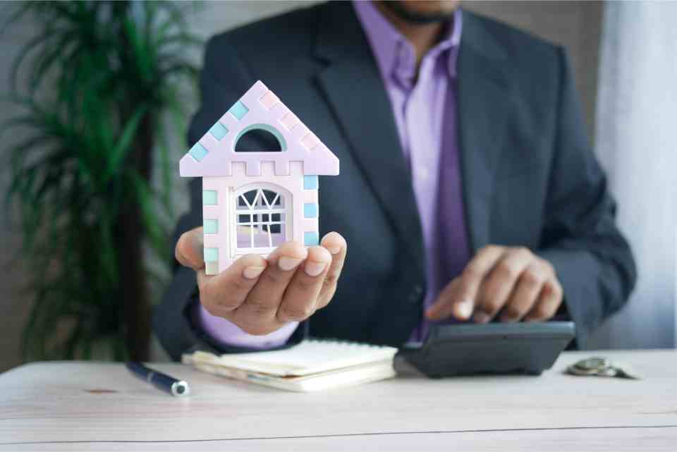 Businessman holding a miniature house for property investment.